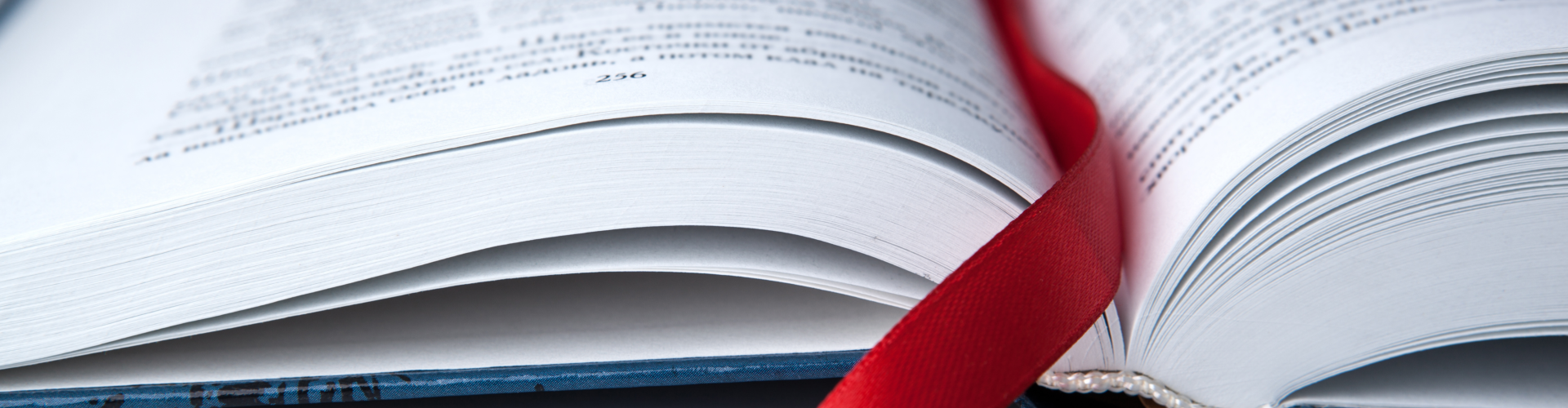 An open book with a red ribbon bookmark lies on a flat surface, showing printed text on its white pages.