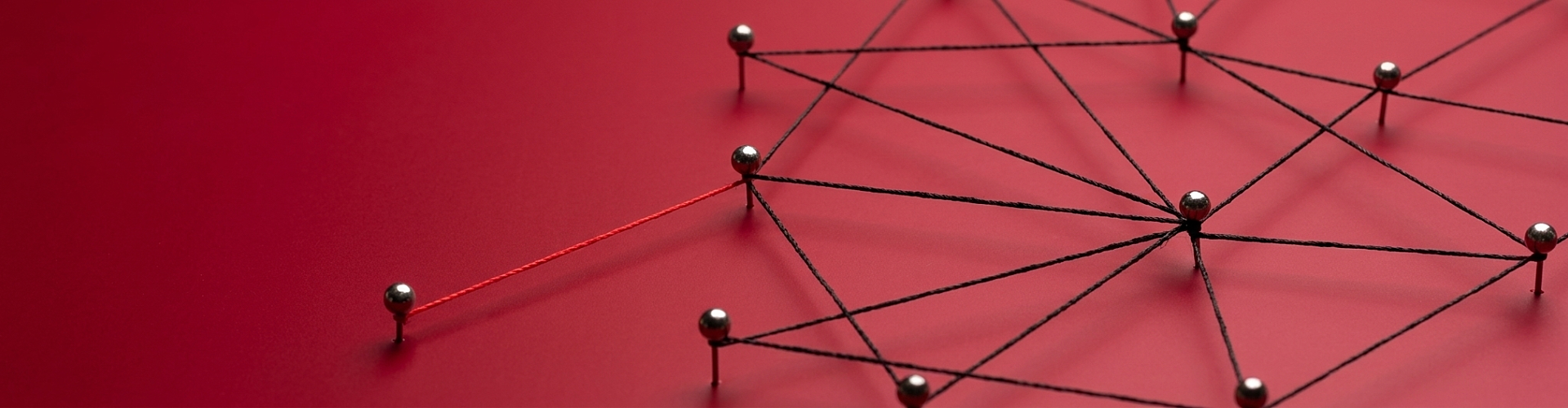 A network of silver pins connected by black string on a red surface, with one pin connected by a single red string.