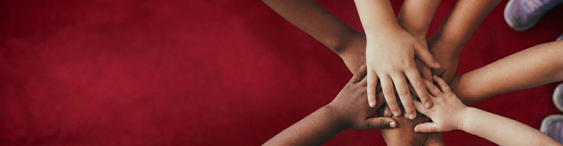 Several hands of different skin tones are stacked together in the center against a red background, suggesting unity and teamwork.