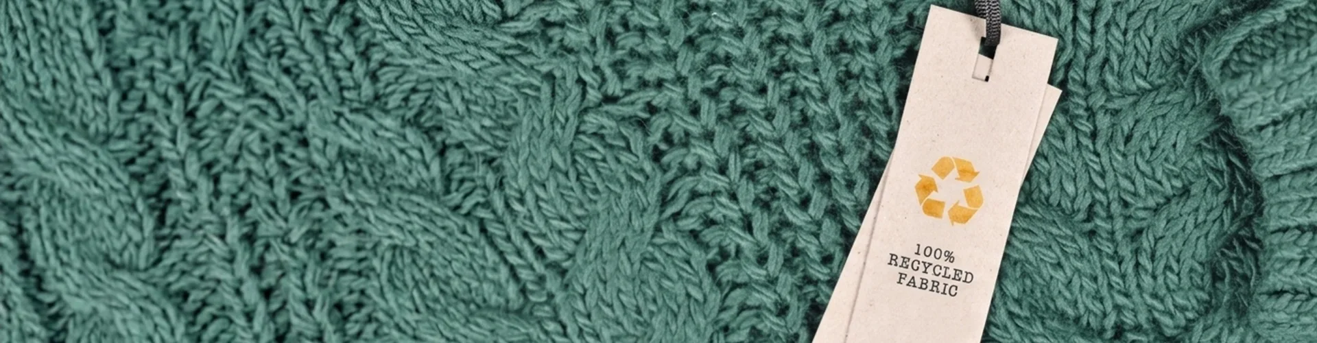Green knitted fabric with a paper tag labeled “100% recycled fabric” and a yellow recycling symbol attached by a black string.