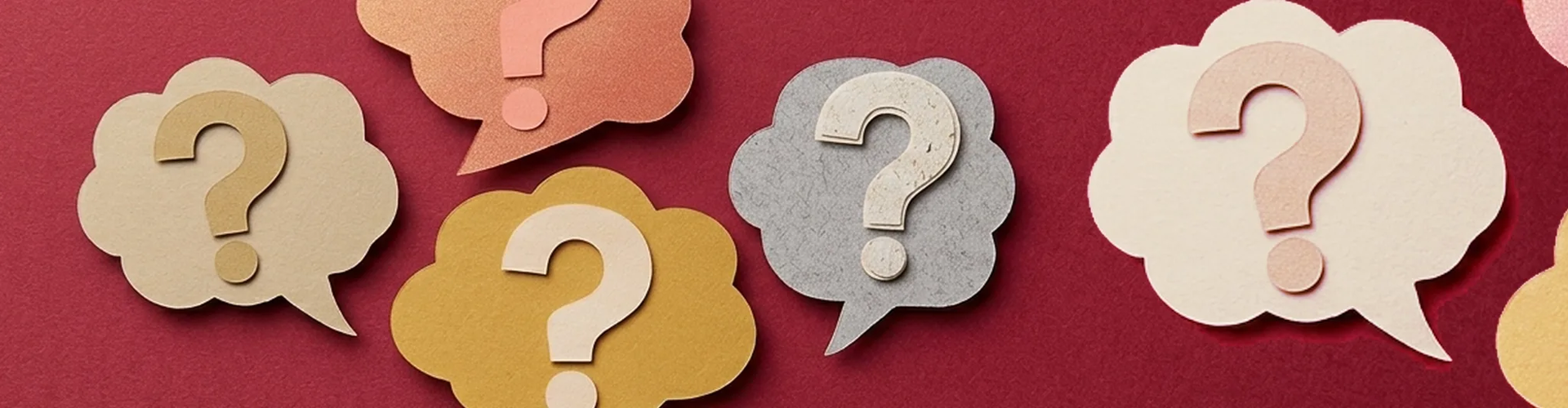 Five paper cutouts of speech bubbles with question marks inside are arranged on a red surface.