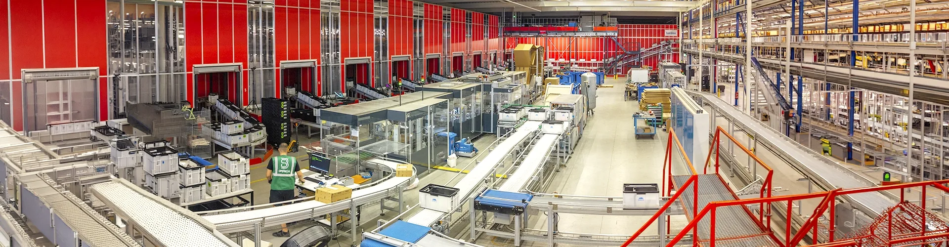 An automated package sorting facility with conveyor belts, sorting stations, and an operator at a computer terminal.