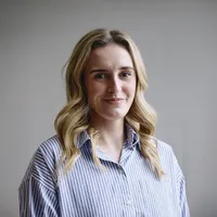 A woman with shoulder-length wavy hair wearing a blue and white striped button-down shirt.
