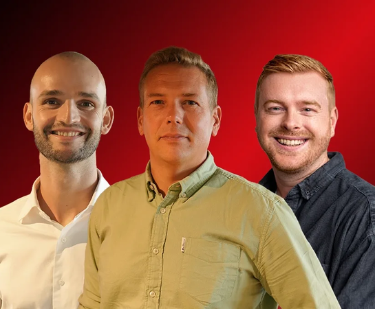 Three men stand side by side, facing forward, in front of a red background. The man in the middle wears a green shirt, while the other two are in white and dark shirts.