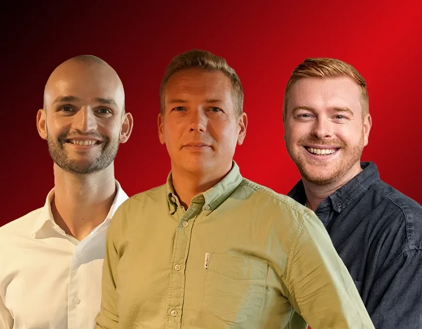 Three men stand side by side, facing forward, in front of a red background. The man in the middle wears a green shirt, while the other two are in white and dark shirts.